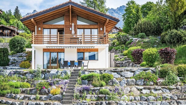 Ein modernes Chalet mit Holzfassade, einem Balkon und einer Steintreppe, die zum Eingang führt.