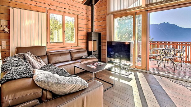 A cozy wooden cabin interior with a leather sofa, a fireplace, and a balcony with a view of mountains. - Stunning private villa for 8 people with WIFI, TV, terrace and panoramic view (Ovronnaz)