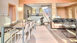 A spacious dining area with a long table and chairs, a kitchen in the background, and a staircase leading to an upper level. - Stunning private villa for 8 people with WIFI, TV, terrace and panoramic view (Ovronnaz)