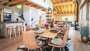 Eine geräumige Küche mit Holzbalken, eine Essecke mit Ledersesseln und ein großer Holztisch, gedeckt für eine Mahlzeit.