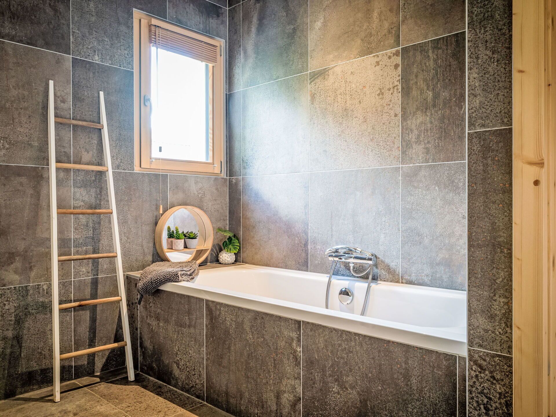 Une salle de bain avec une baignoire, une échelle en bois et une fenêtre.
