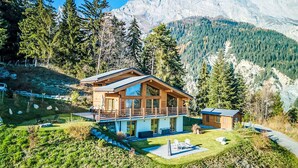 Eine moderne Holzdiele mit Balkon, umgeben von einem gepflegten Rasen und Blick auf die Berge.
