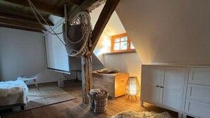 Ein gemütliches Schlafzimmer im Dachgeschoss mit Holzboden, einem Fellteppich, einem Korb, einem kleinen Tisch und einem Fenster mit Tageslicht.