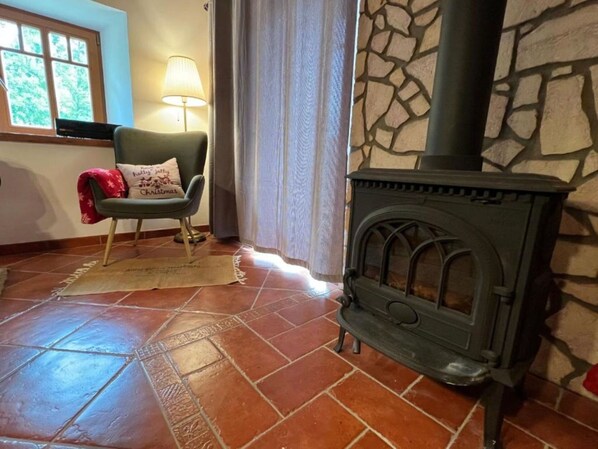 Una habitación acogedora con pared de piedra, chimenea, un sillón y una lámpara, además de un cojín navideño.