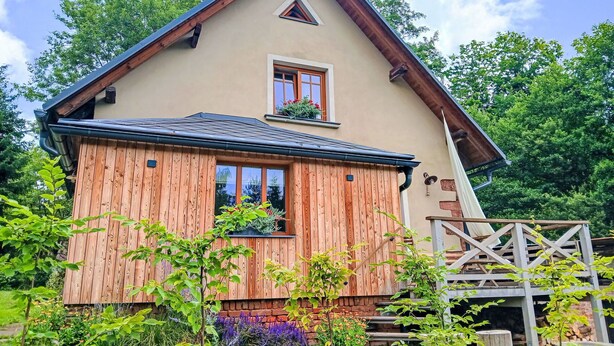 Ein zweistöckiges Haus mit Holzfassade, kleinem Balkon und einem sichtbaren Schornstein.
