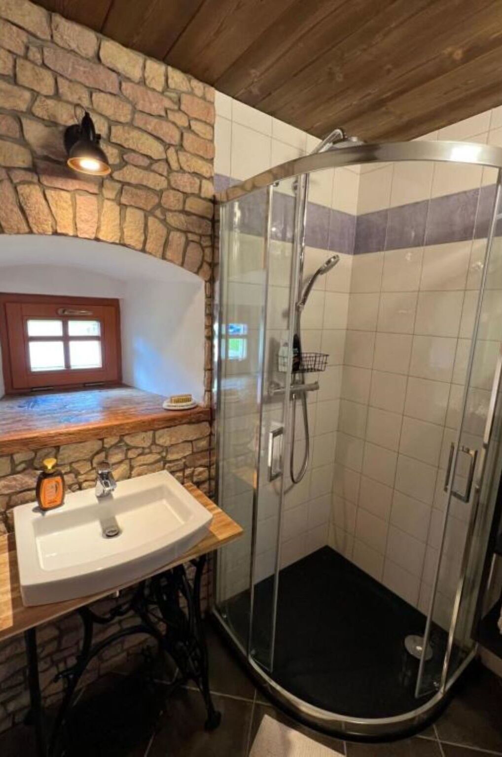 Une salle de bain avec un mur en pierre, un lavabo et une douche fermée par des parois de verre.