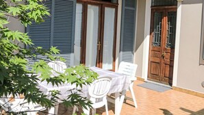 Un patio con mesa y sillas, una puerta de madera y una ventana con contraventanas azules.