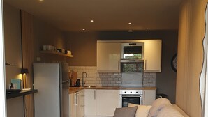 A compact kitchen with a refrigerator, oven, microwave, and a sink. A white sofa with cushions is placed in the living area. - Apartment 2 pers Residence PISCINE Mandelieu La Napoule Beaches 15mn walk (Mandelieu-la-Napoule)