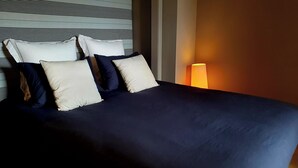 A neatly made bed with dark blue bedding and multiple pillows, a striped headboard, and a bedside lamp. - Apartment 2 pers Residence PISCINE Mandelieu La Napoule Beaches 15mn walk (Mandelieu-la-Napoule)