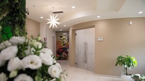 A reception area with a green wall, a white flower arrangement, a potted plant, and a marble wall. - Lual Bleisure Hotel  (Pofi)