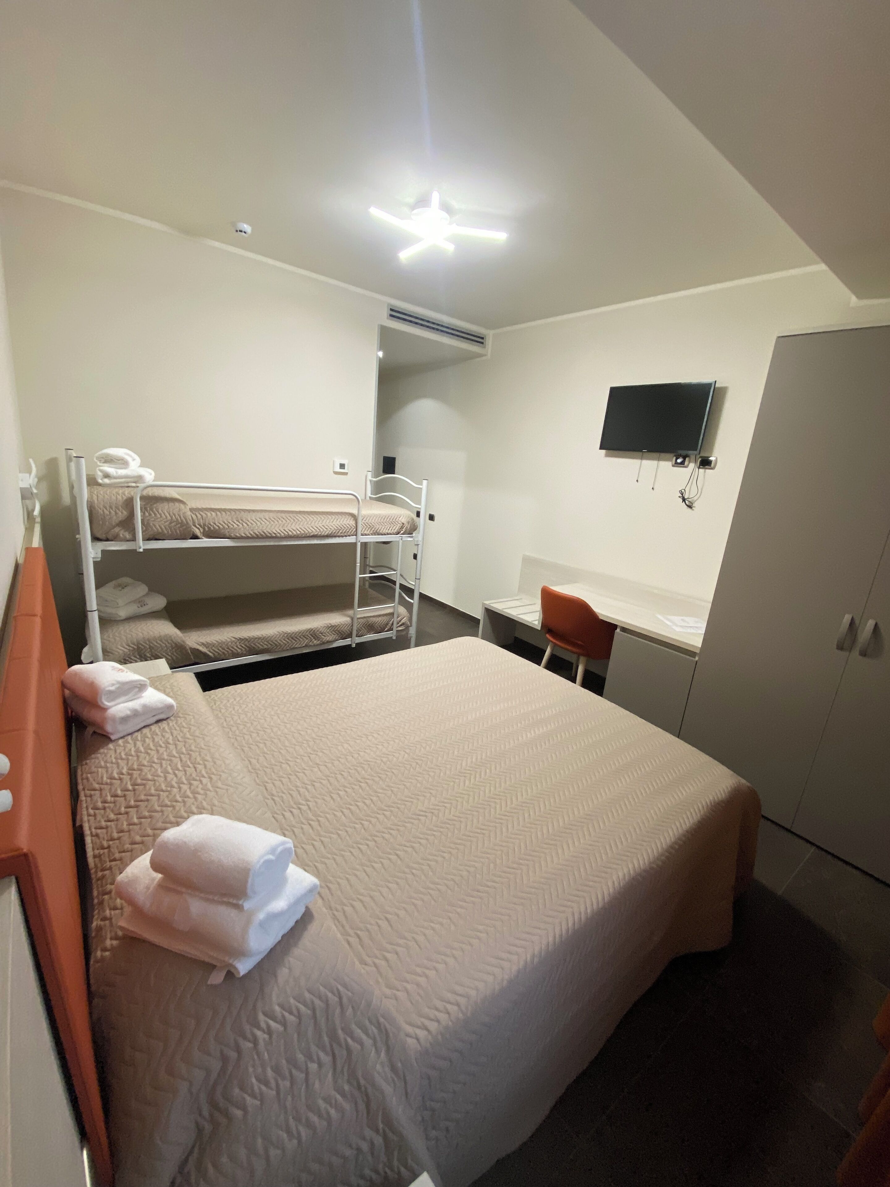 A hotel room with a bunk bed, a desk, a TV, and a wardrobe.
