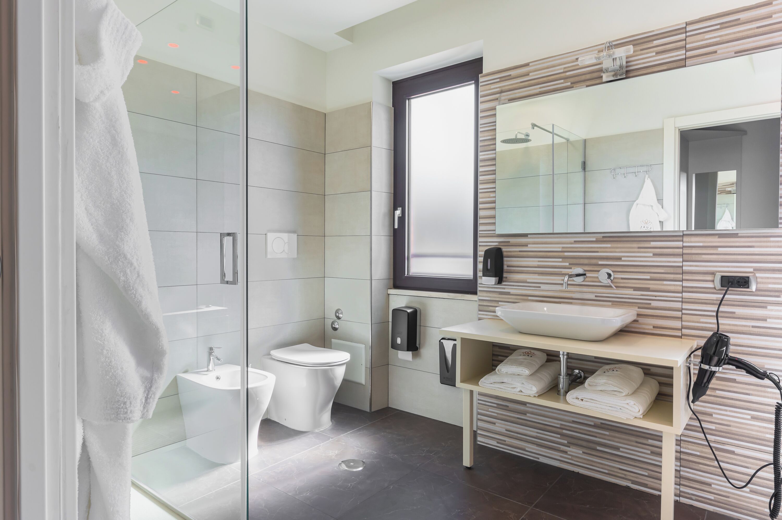 Un baño moderno con cabina de ducha de vidrio, un lavamanos blanco y un mueble de tocador con toallas.