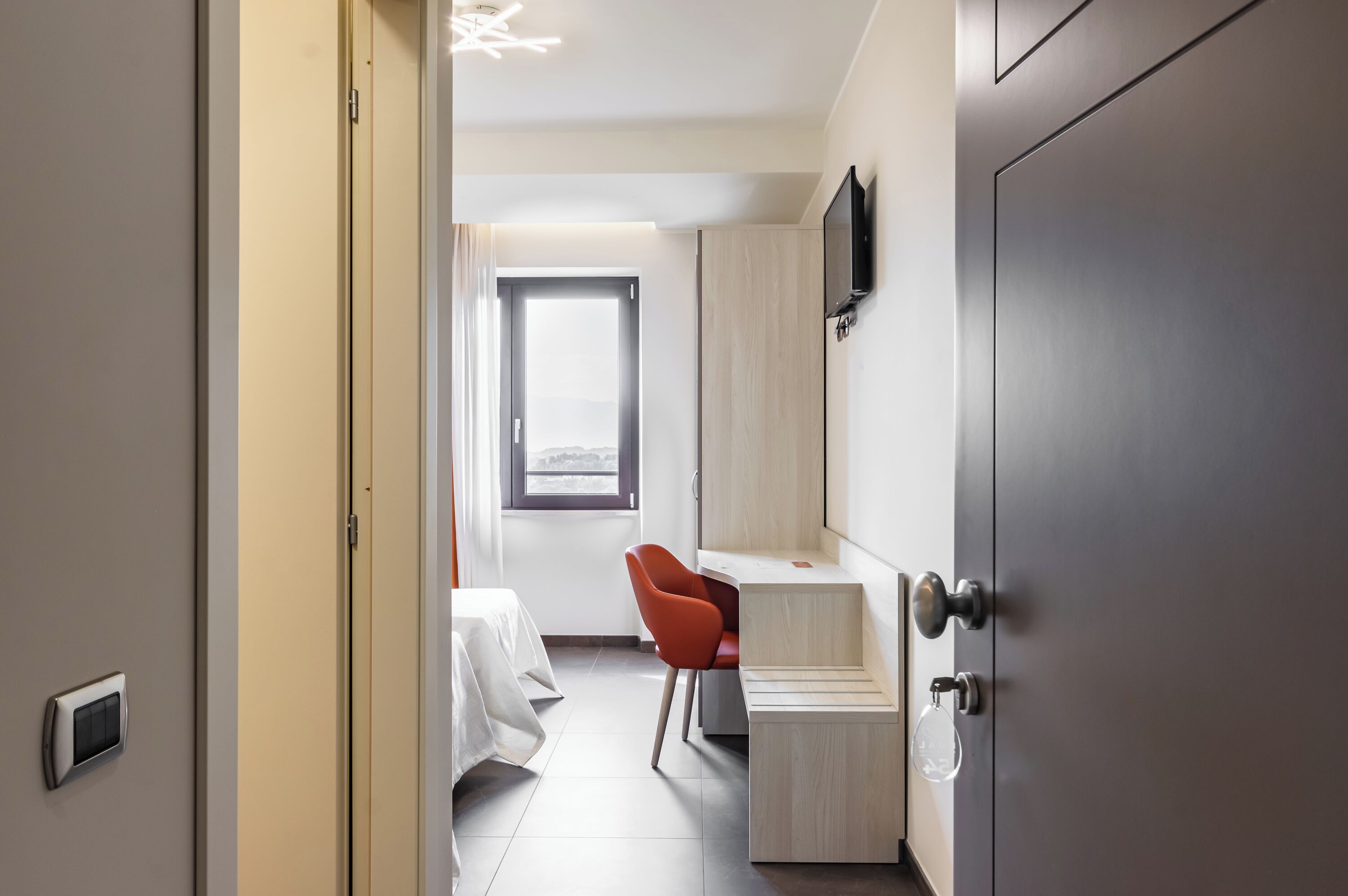 A modern hotel room with a bed, a desk, a chair, a TV, and a wardrobe.