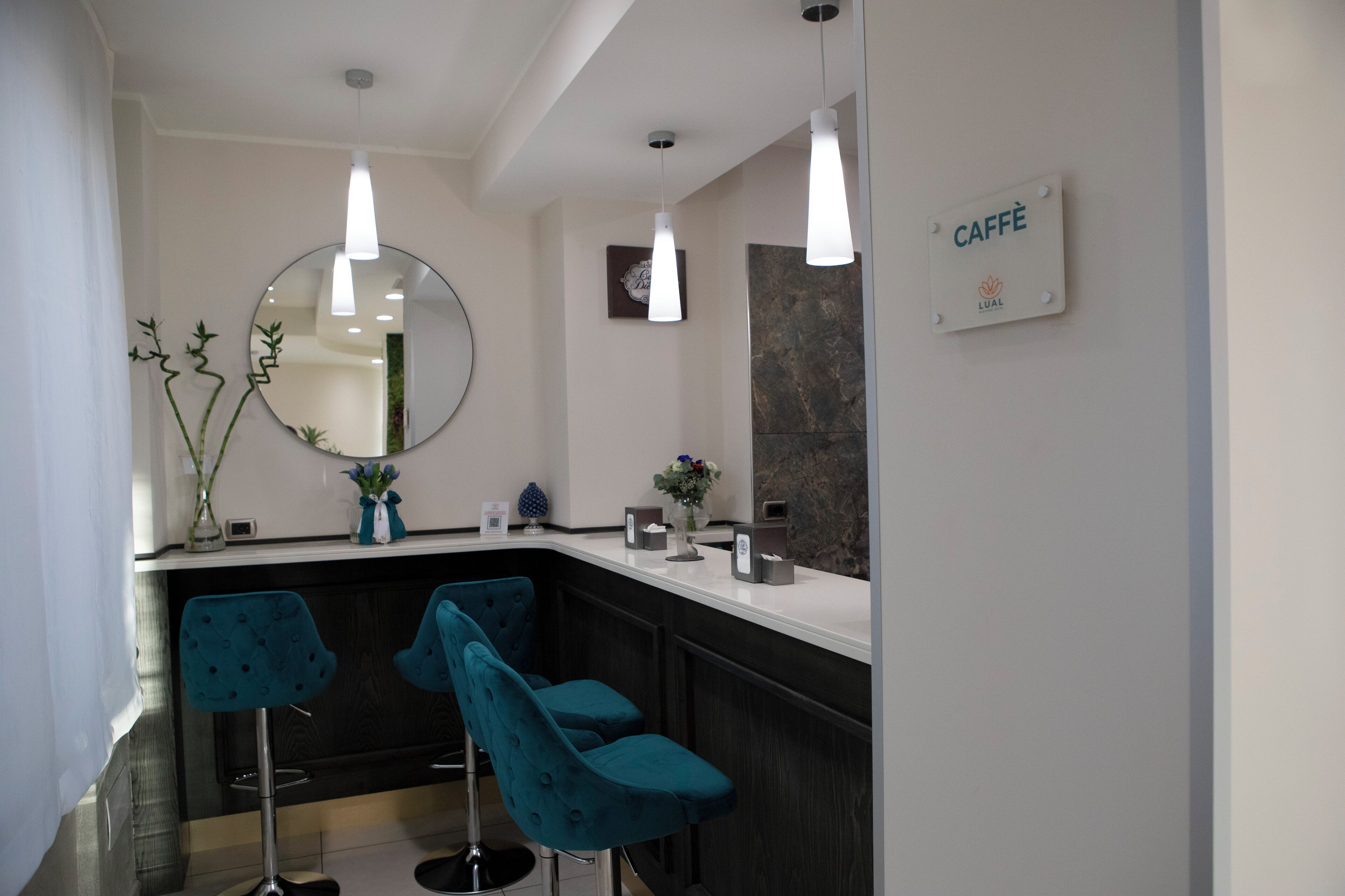 Un baño moderno con espejo, dos lámparas colgantes, una barra tipo mostrador y dos taburetes turquesa.