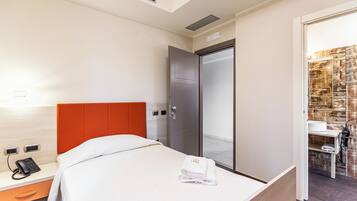Habitación de hotel con cama, mesita de noche con teléfono, y baño con espejo y toallero.