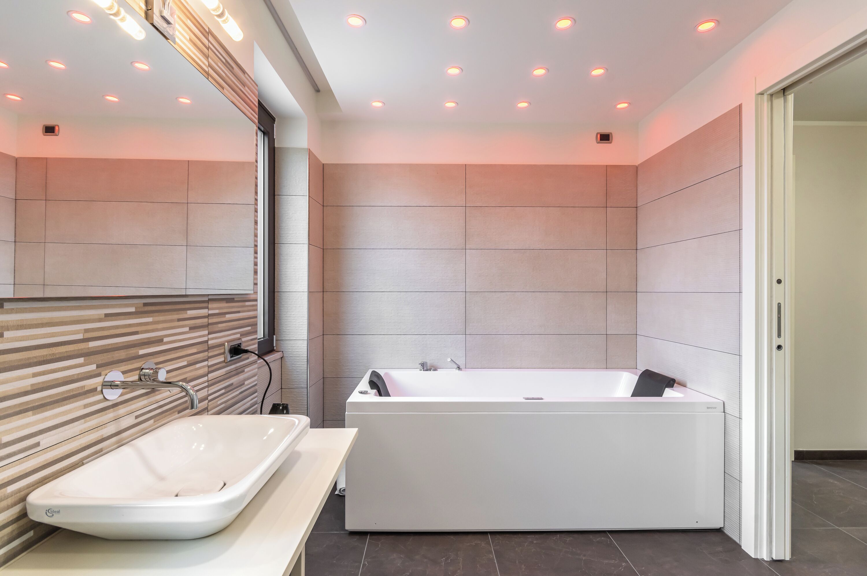 Een moderne badkamer met een groot bad, een wastafelmeubel en inbouwspots.
