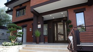 A modern building with a brick facade, a set of beige steps leading to a glass door entrance, and a sign indicating the name 'LUAL'. - Lual Bleisure Hotel  (Pofi)
