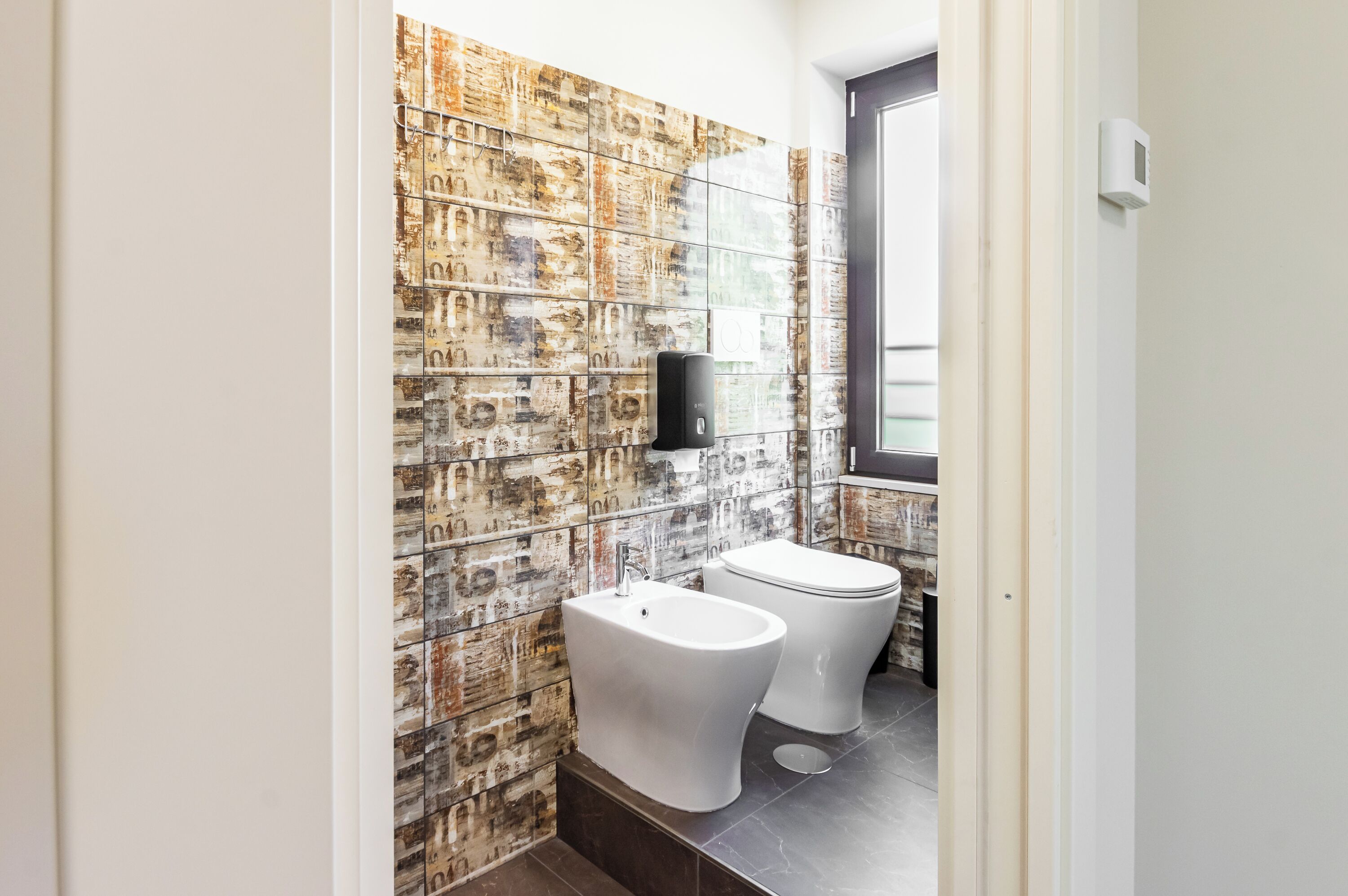 Een badkamer met een wand van mozaïektegels, een bidet, een toilet en een handdroger.