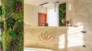 A reception area with a moss-covered wall, a lotus symbol, and a reception desk with a computer and decorative items. - Lual Bleisure Hotel  (Pofi)