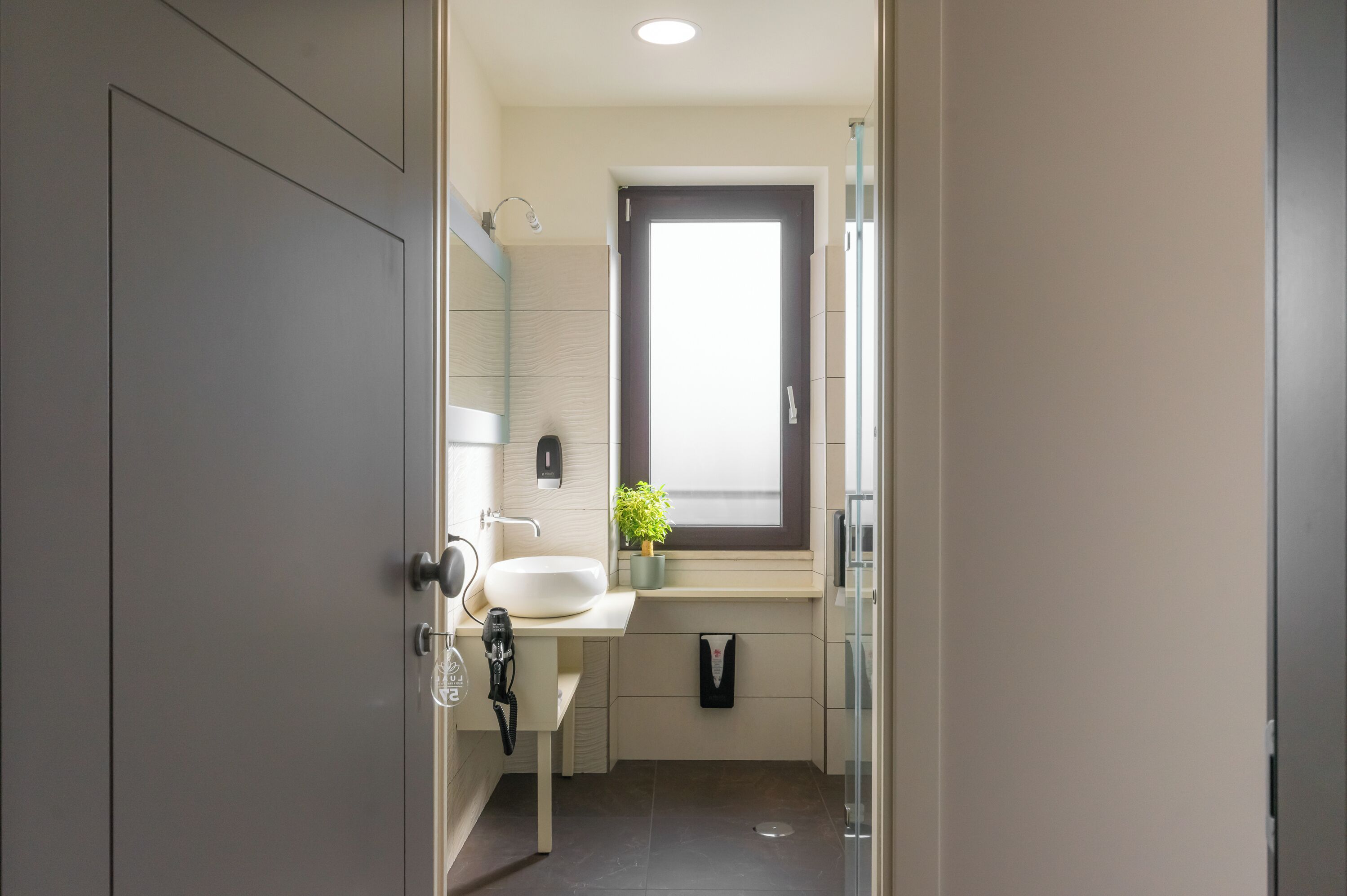 Un baño moderno con un espejo grande, un lavabo blanco, una ventana pequeña y un perchero para toallas.