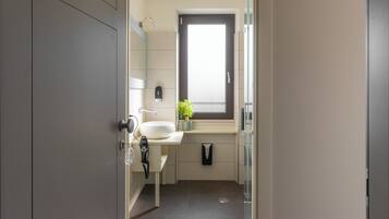 Un baño moderno con un espejo grande, un lavabo blanco, una ventana pequeña y un perchero para toallas.