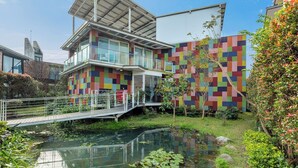 A modern building with a colorful facade, a small bridge, and a pond with lily pads. - BoxDuoDuo (Wujie)