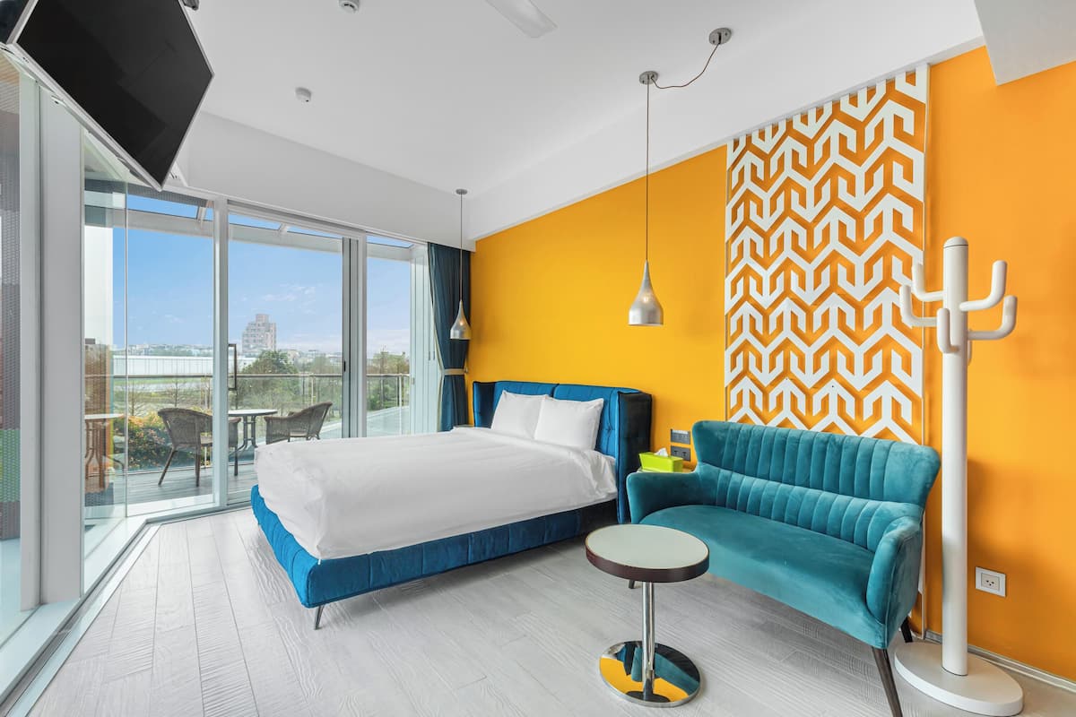 Una habitació d'hotel moderna amb un llit gran, un sofà blau, una taula rodona petita i un gran finestral que ofereix una vista de la ciutat.