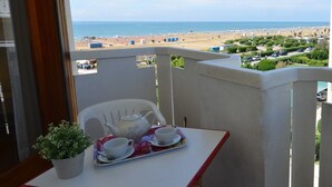 Un balcón con una mesa lista para el té, una planta en maceta y vistas a la playa y al paisaje urbano.