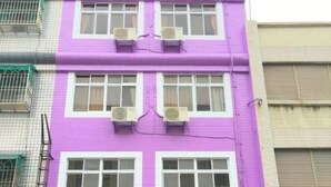 Un edificio de varios pisos con fachada morada, ventanas amplias y una entrada a nivel de calle con puerta de vidrio.