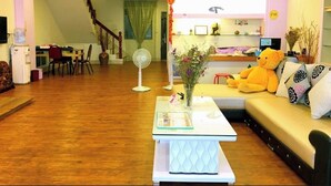 Sala de estar con sofá, una mesa de centro, un ventilador y un oso de peluche. Se ve una escalera al fondo.