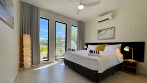 Quarto moderno com uma cama grande, ventilador de teto e vista através das portas de correr de vidro.