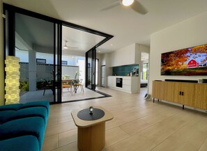A modern living room with a blue sofa, a coffee table, and a TV mounted on the wall. - Palm Cove 2 bedroom new built with large heated spa (Palm Cove)