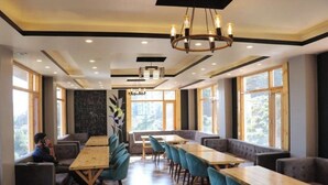 A modern dining area with long tables and comfortable seating, large windows offering views, and a chandelier. - Uno Prime shimla (Shimla)