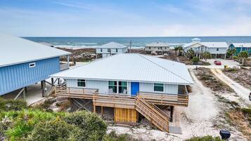 A coastal building with a blue exterior, wooden deck, and a staircase leading to a door.