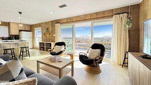 A modern living room with a sofa, two armchairs, a coffee table, and a kitchen area with a fridge and bar stools. - Beautiful Views Easy Beach & Bay Access (Gulf Shores)