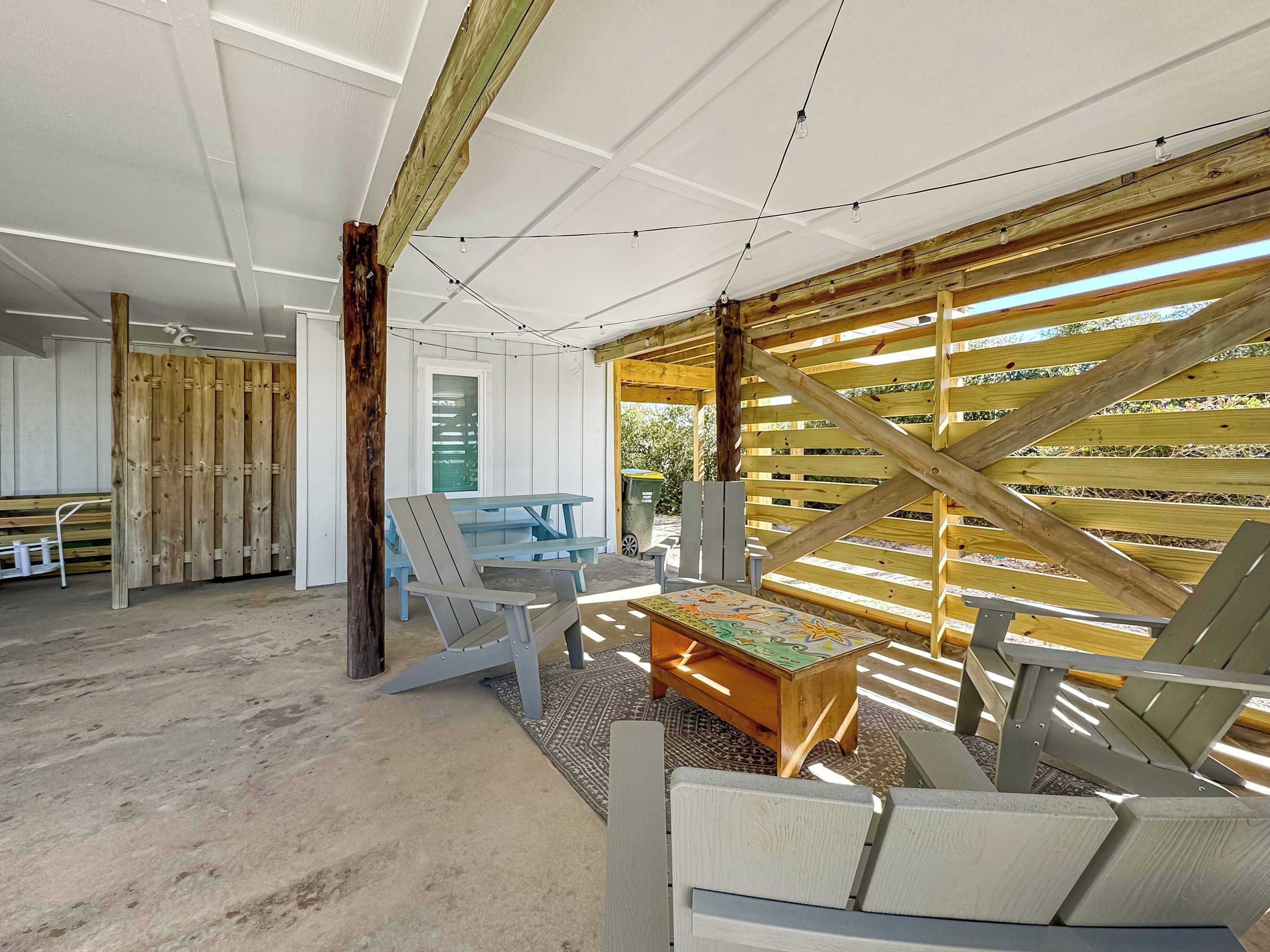 A spacious room with a large wooden table, several Adirondack chairs, and a view through a wooden slatted wall.