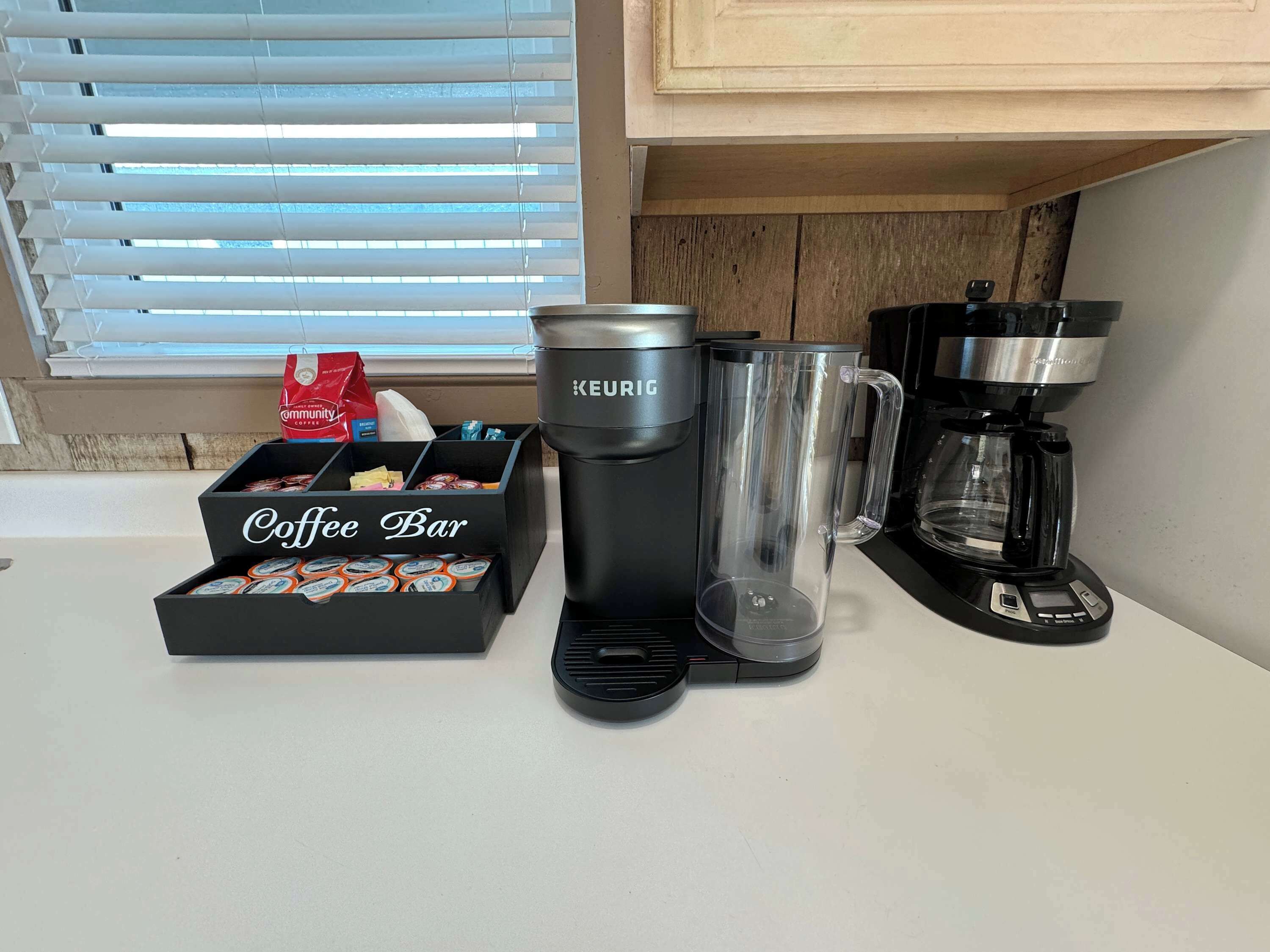 A coffee bar setup with a Keurig coffee maker, a glass mug, and a coffee pod box labeled "Coffee Bar".