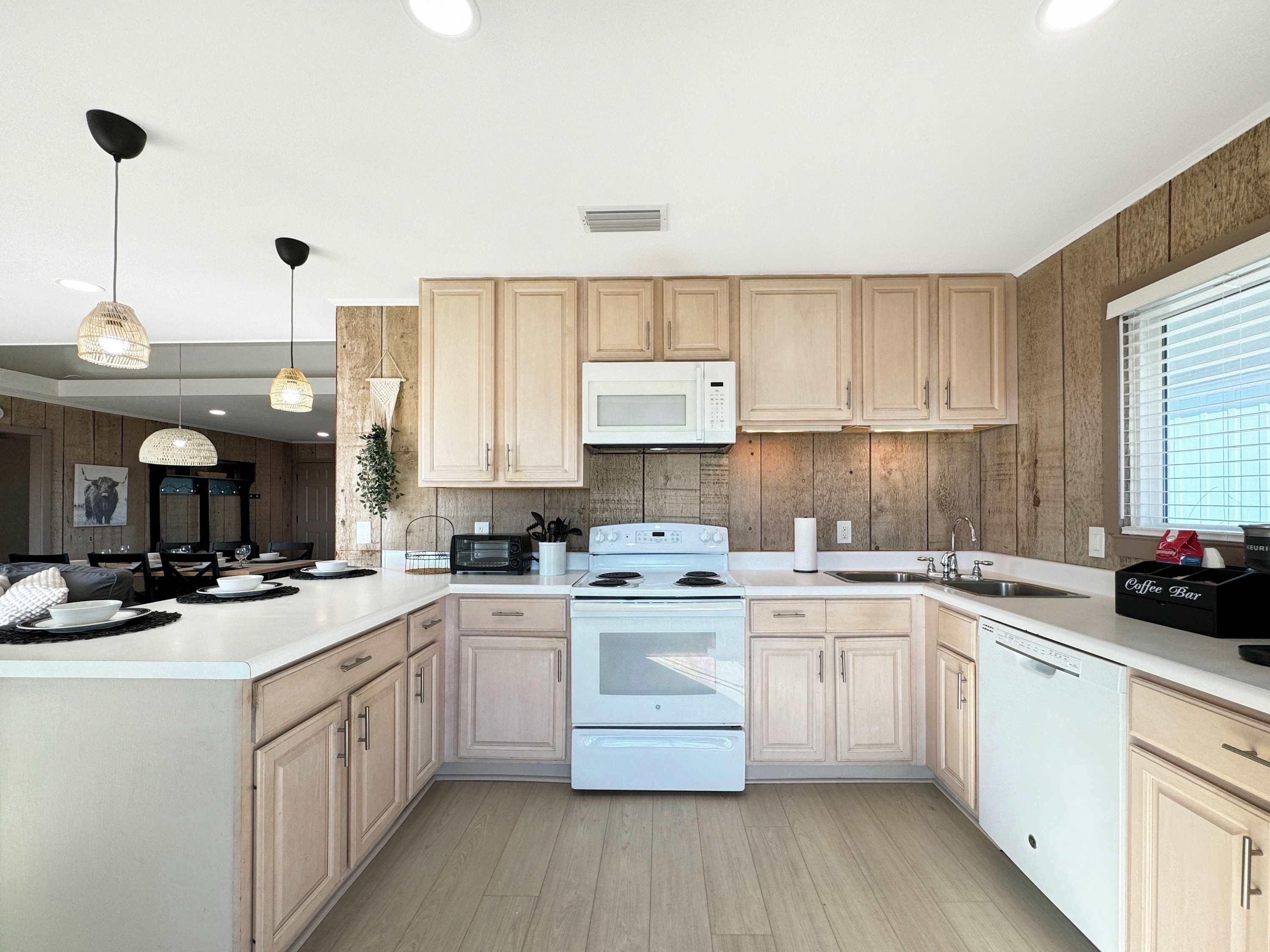 Une cuisine moderne avec des meubles en bois, une cuisinière blanche, un four à micro-ondes et des luminaires suspendus.