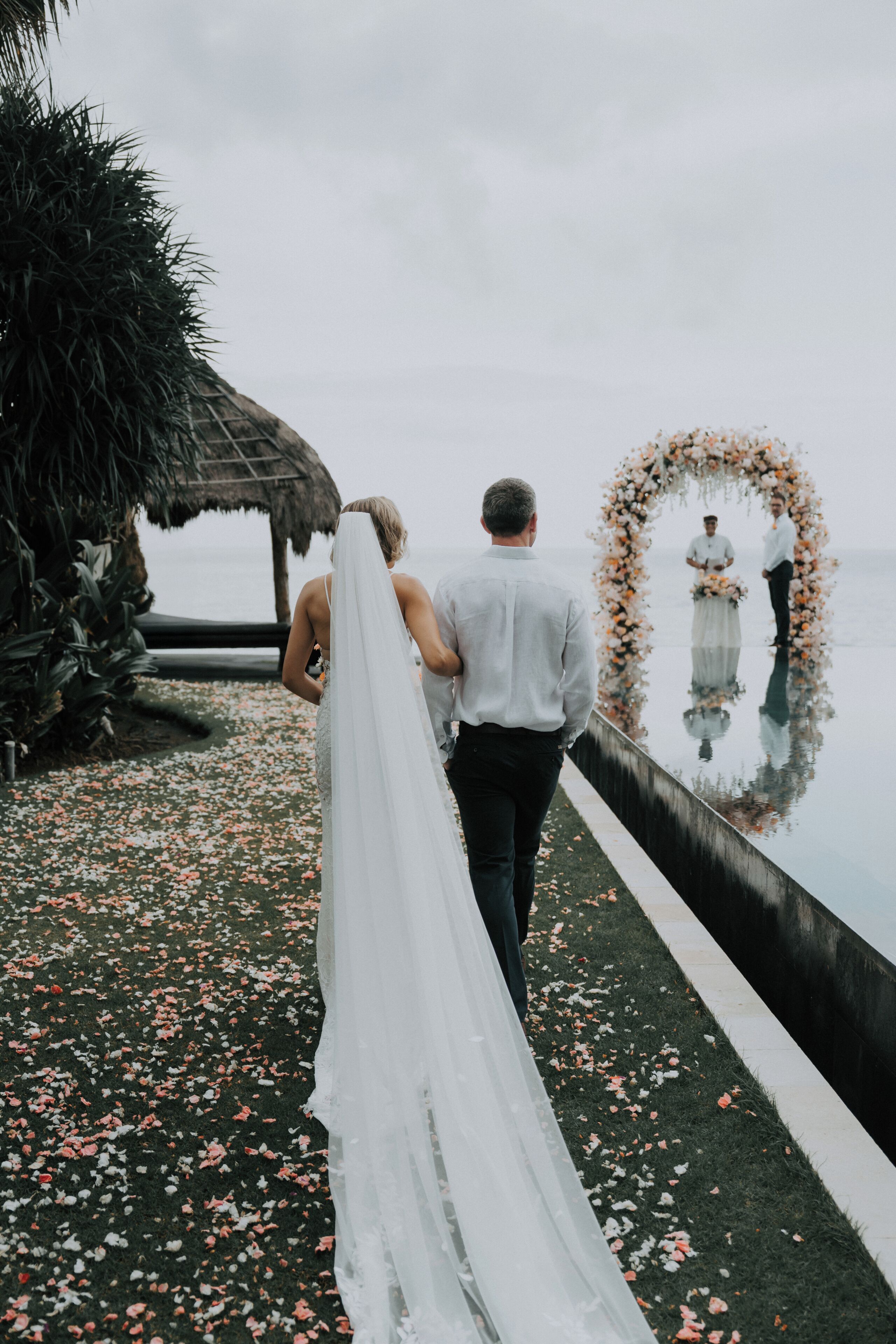 Ein Paar geht auf eine Hochzeitsecke zu, neben einer spiegelnden Wasseroberfläche.