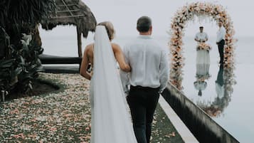 Ein Paar geht auf eine Hochzeitsecke zu, neben einer spiegelnden Wasseroberfläche.