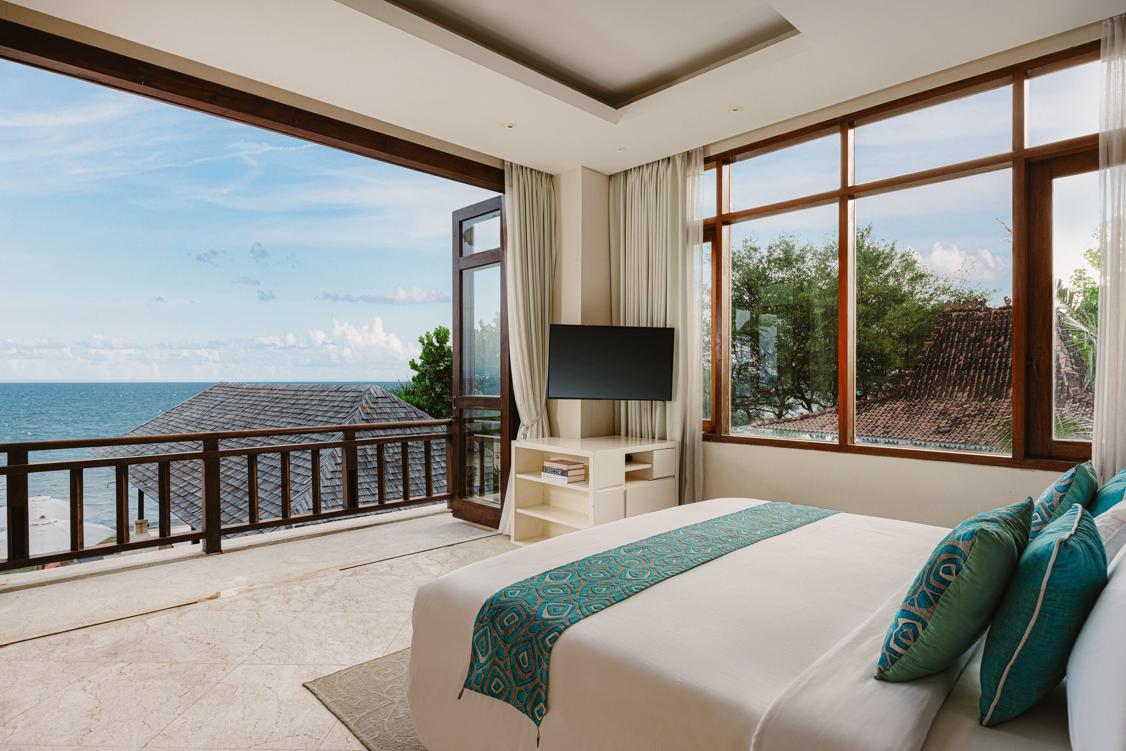 Habitación de hotel con una cama grande, un televisor en un mueble bajo y un balcón con vistas al mar.