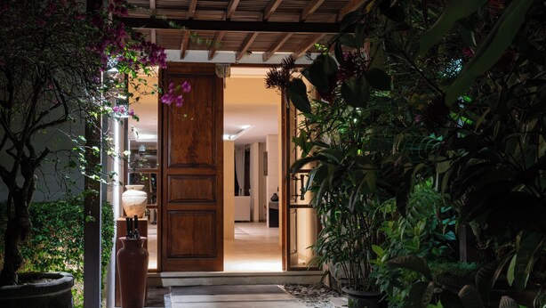 Una puerta de madera que da a un espacio interior bien iluminado, con suelo de baldosas y plantas en macetas.