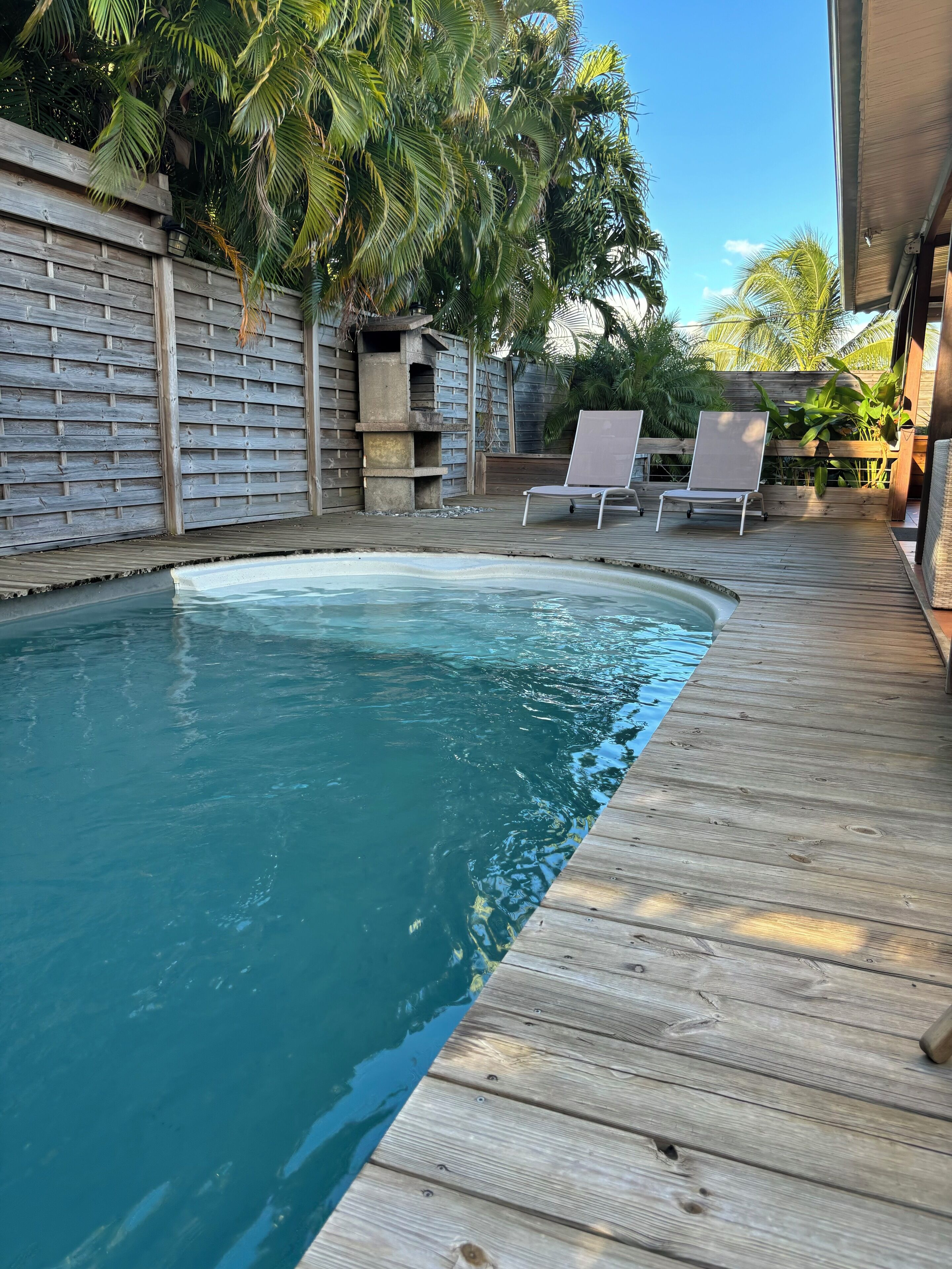 A wooden deck surrounding a swimming pool with lounge chairs and a wooden fence with plants.