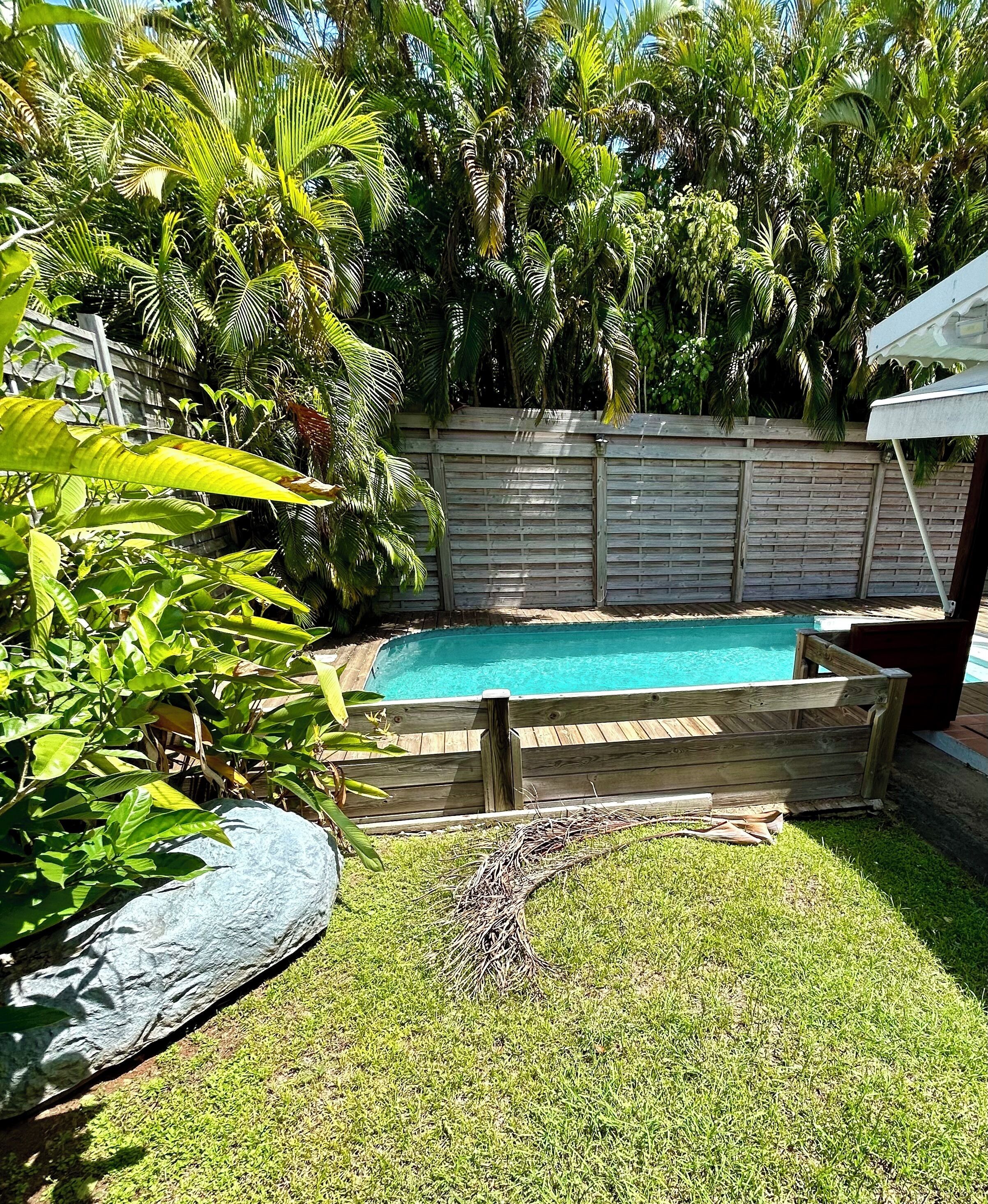 A backyard with a swimming pool, surrounded by lush greenery and a wooden fence.