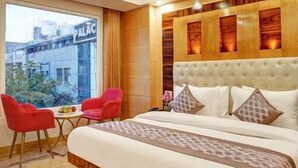 A modern hotel room with a large bed, a ceiling fan, a view of the outside, and a small table with chairs. - Hotel Lord Krishna Palace  (New Delhi)