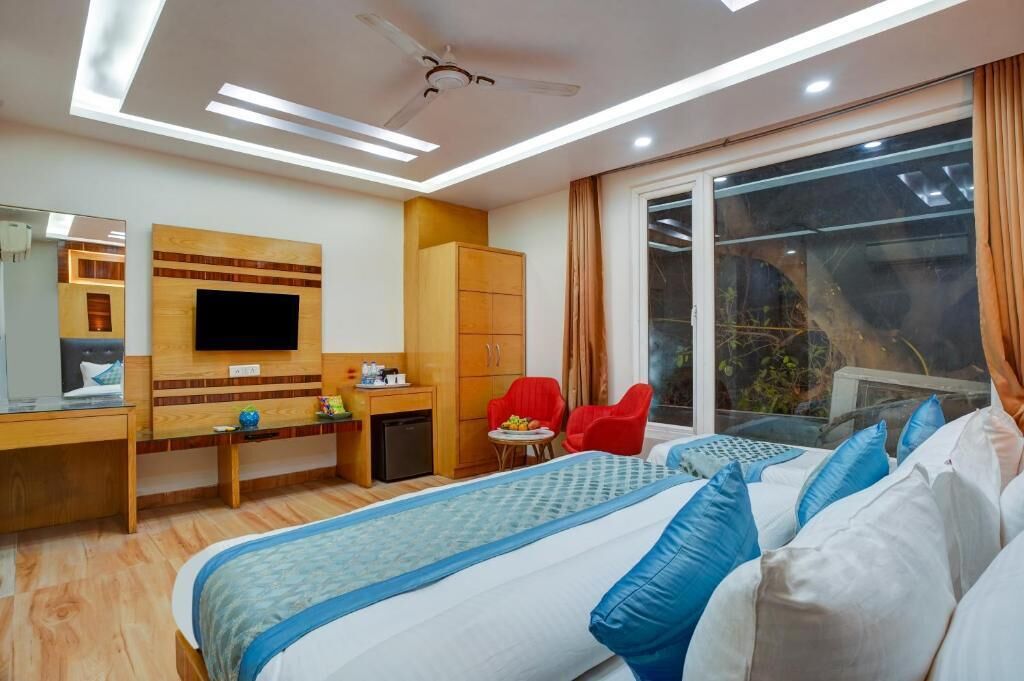 A hotel room with a bed, a desk, a television, a wardrobe, and a window with a view of greenery.