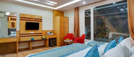 A hotel room with a bed, a desk, a television, a wardrobe, and a window with a view of greenery.