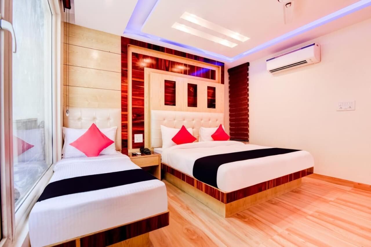 A hotel room with two beds, a wooden floor, a large window, and a modern ceiling design.