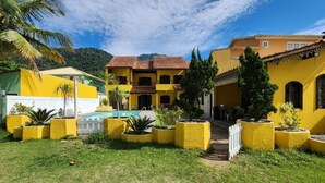 Ein Innenhof mit gelben Gebäuden, einem Pool und viel Grün.