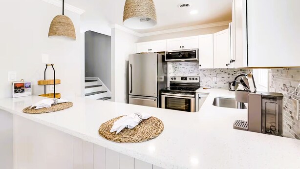 A modern kitchen with white cabinetry, stainless steel appliances, and woven pendant lights.